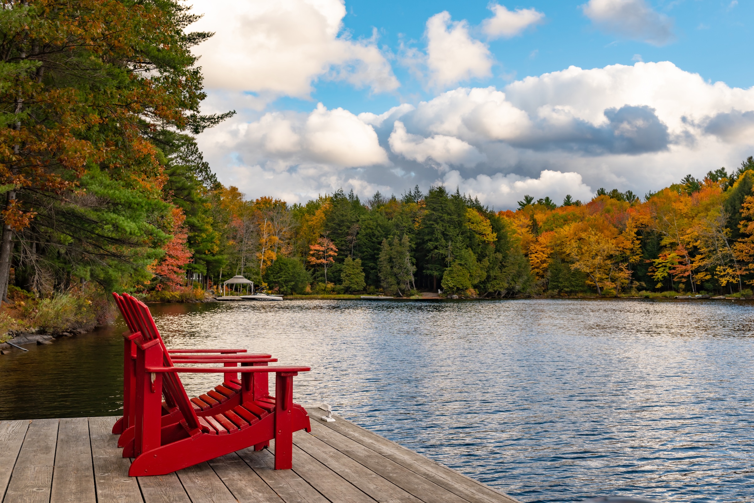 Chaises Adirondack rouges sur un quai au bord d’un lac au Québec, entouré de couleurs d’automne.