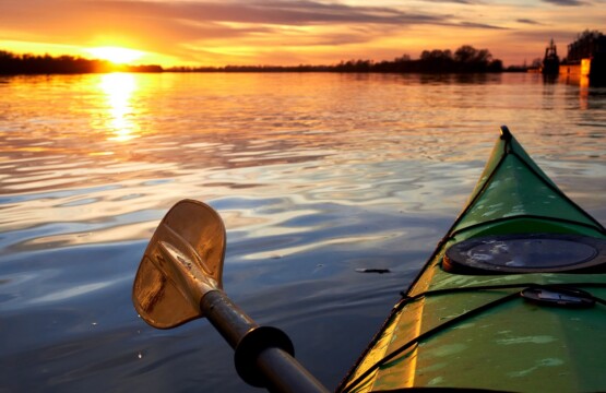 Kayak vert avec pagaie orangée sur un cours d'eau au coucher de soleil