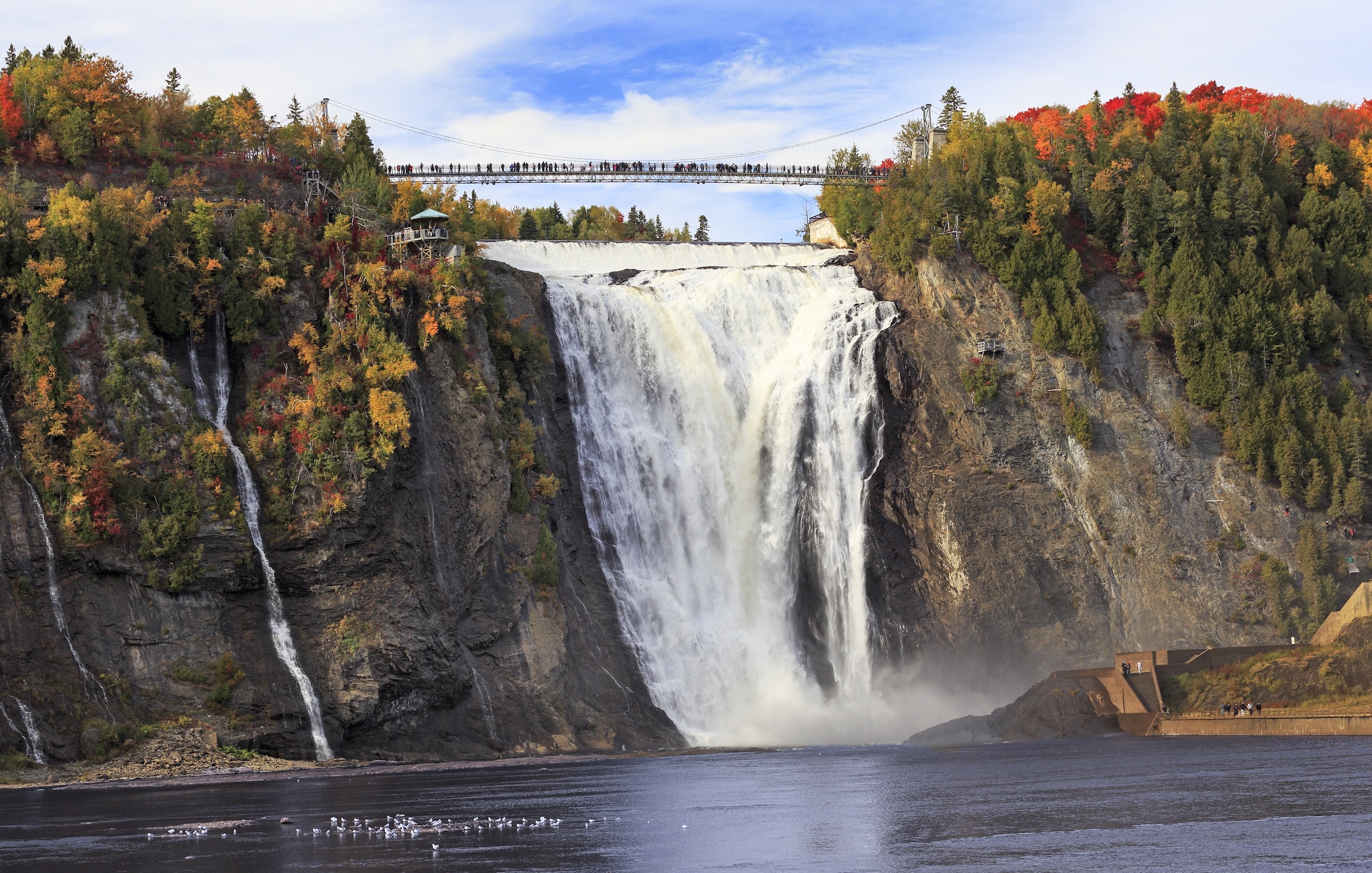 View of Montmorency Falls surrounded by fall colours, with the suspension bridge above the waterfall.